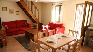 A dining area with a wooden table and chairs, a red sofa, a staircase, and a window with curtains.
