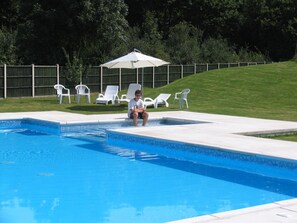 A swimming pool with a tiled edge, surrounded by white lounge chairs and a covered umbrella. - Aspace 3* 2 bedroom gites with large pool, fun games area,Many local attractions (La Ferrière-en-Parthenay)