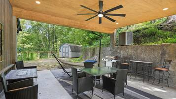 Eine Terrasse im Freien mit Deckenventilator, Grill und Korbmöbeln.