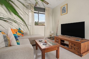 Ein Wohnzimmer mit einer Couch, einem Couchtisch, einem Fernseher und einem Fenster mit Vorhängen.