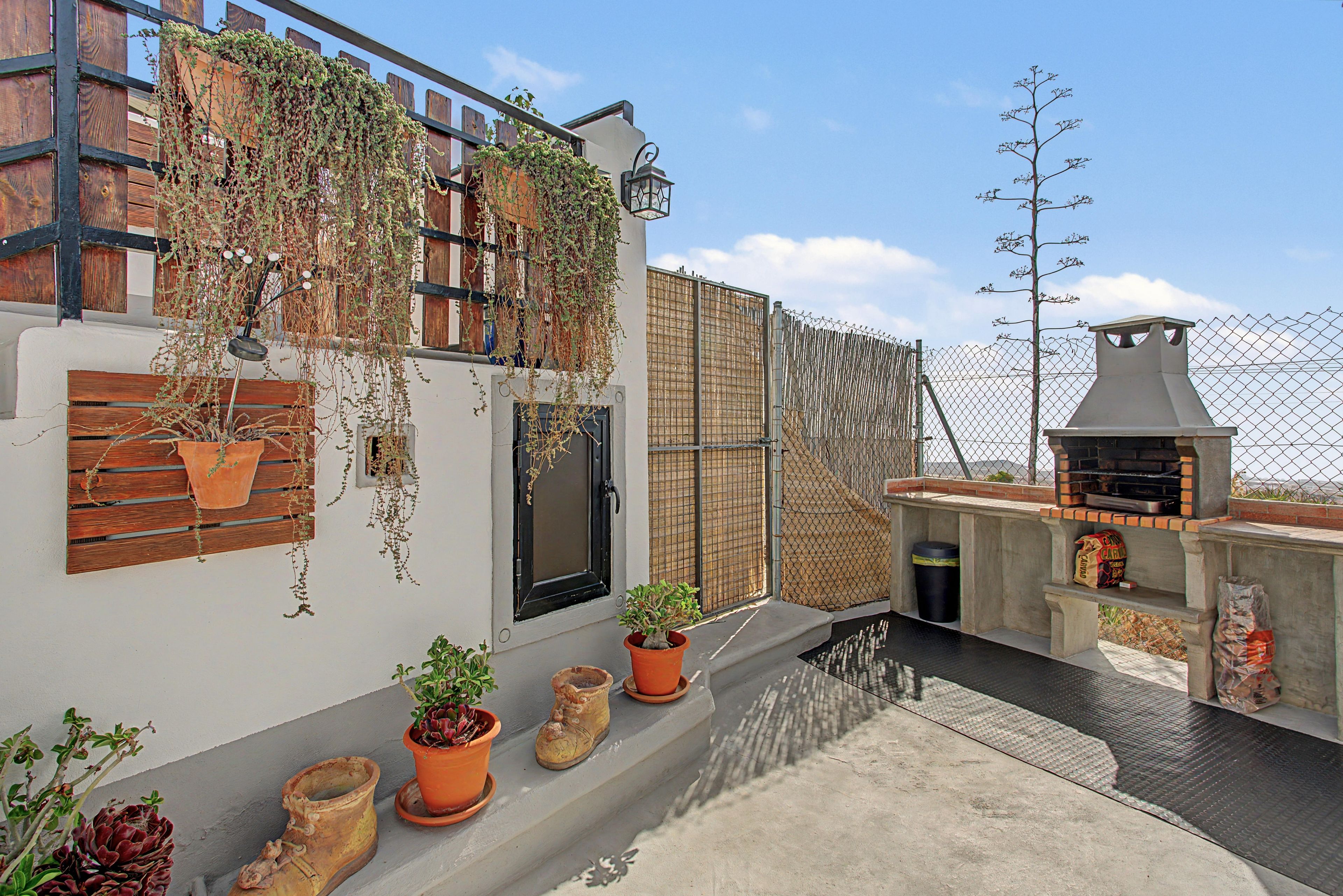 A rooftop terrace with a barbecue grill, potted plants, and a wooden fence.