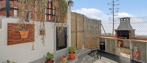 A rooftop terrace with a barbecue grill, potted plants, and a wooden fence.