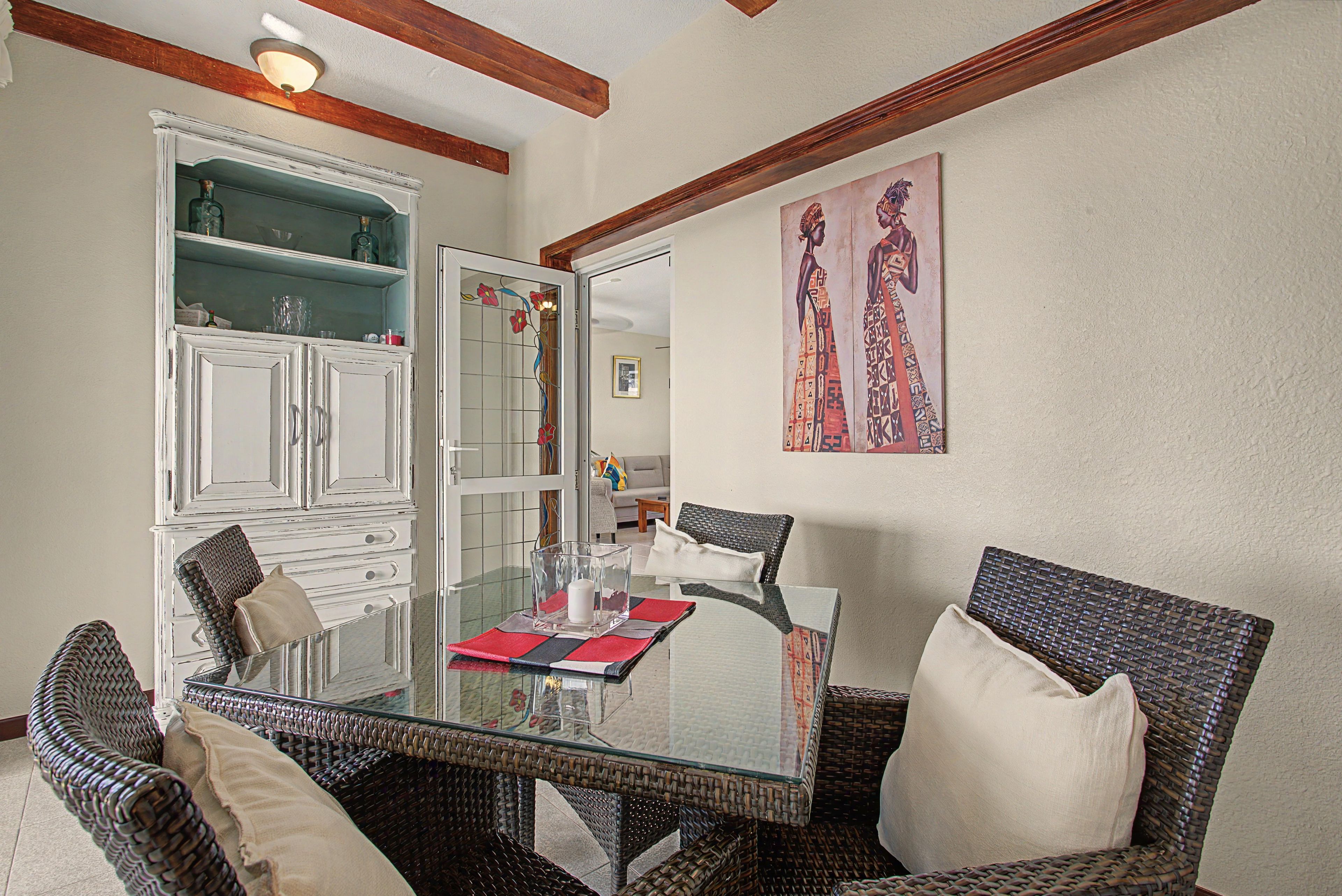 A dining area with a glass table, wicker chairs, and a cabinet with glass doors.