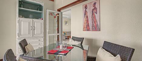 A dining area with a glass table, wicker chairs, and a cabinet with glass doors.