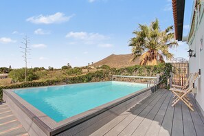 A rectangular swimming pool with a wooden deck and metal railings, surrounded by greenery and a mountain in the background. - Vacation Home 'Casa Colina Tenerife' with Sea View, Balcony and Wi-Fi (Granadilla de Abona)