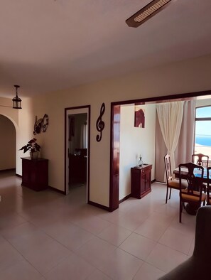 Ein geräumiges Wohnzimmer mit Esstisch, Stühlen, einer Topfpflanze und Blick auf das Meer.