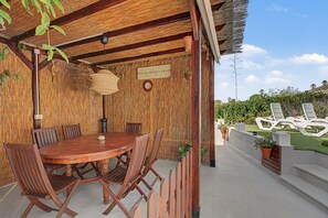 Ein Essbereich im Freien mit Holztisch und -stühlen, einer hängenden Leuchte und einer Wand mit Bambusstruktur.