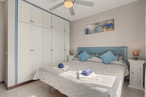 Ein Schlafzimmer mit einem Bett, einem Deckenventilator, einem Nachttisch und einem Wandbild.