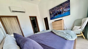 Un dormitorio con cama, televisor montado en la pared, armario de madera y una silla.