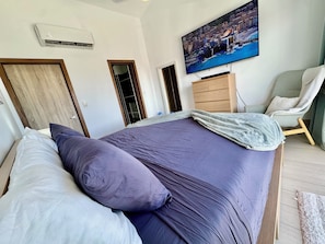 A bedroom with a bed, a television mounted on the wall, a wooden wardrobe, and a chair. - Gold Coast Luxury Sea View, High-End Amenities (Punta Cana)