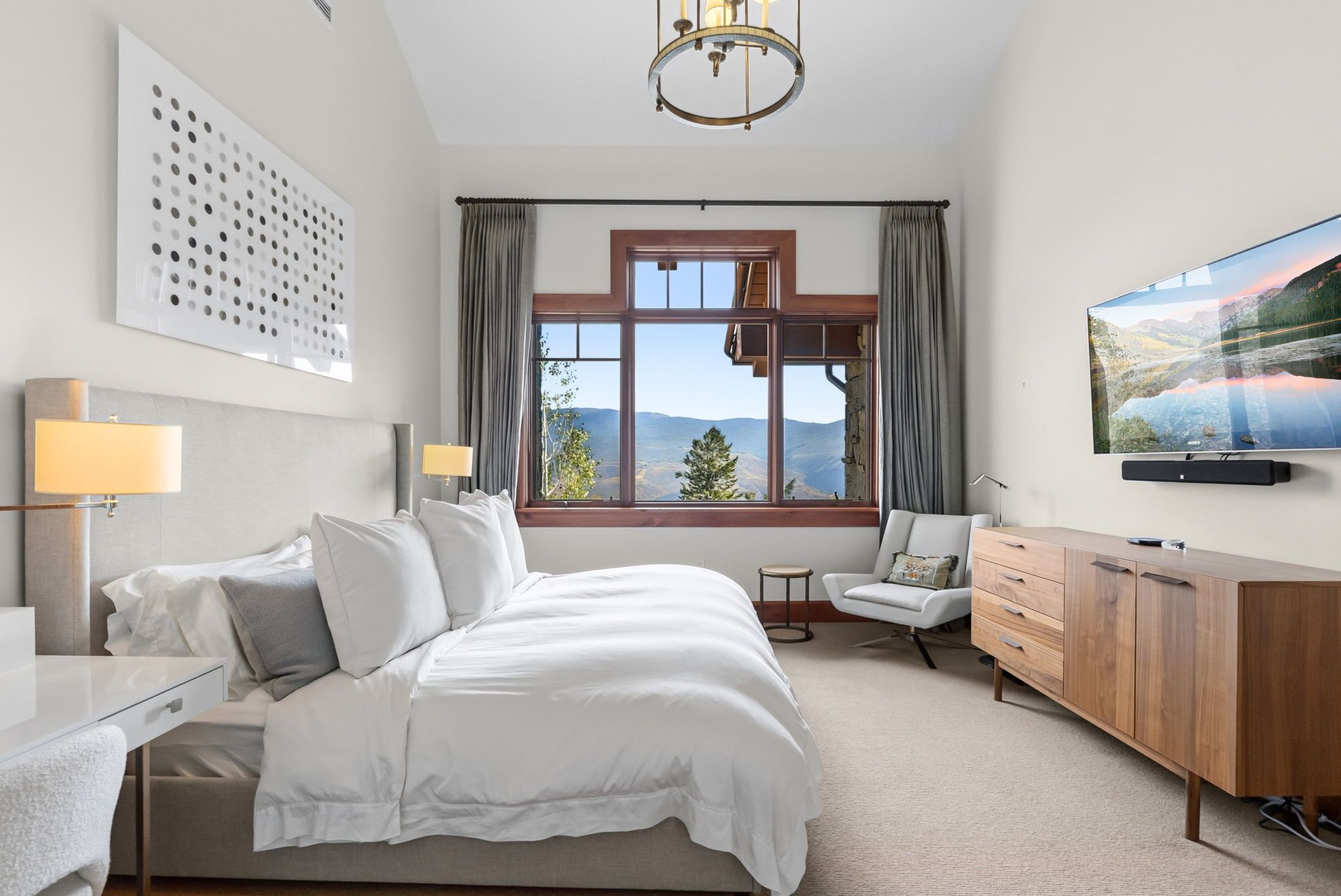 Une chambre d’hôtel avec un grand lit, un bureau, une chaise, une télévision et une fenêtre donnant sur les montagnes.