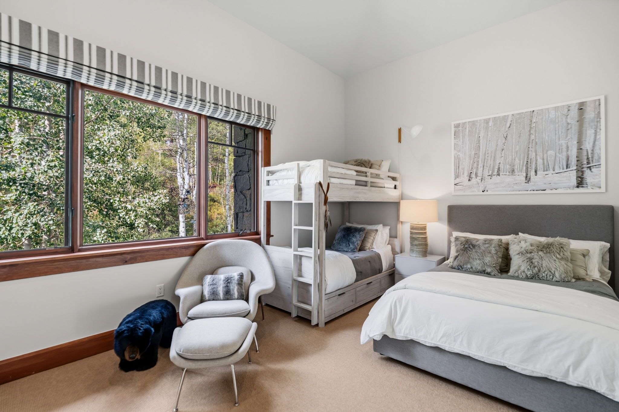 Un dormitorio con una cama individual alta, un escritorio, una silla y una cama. Hay una ventana con vistas a árboles.
