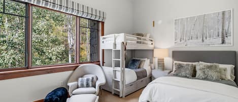 Un dormitorio con una cama individual alta, un escritorio, una silla y una cama. Hay una ventana con vistas a árboles.