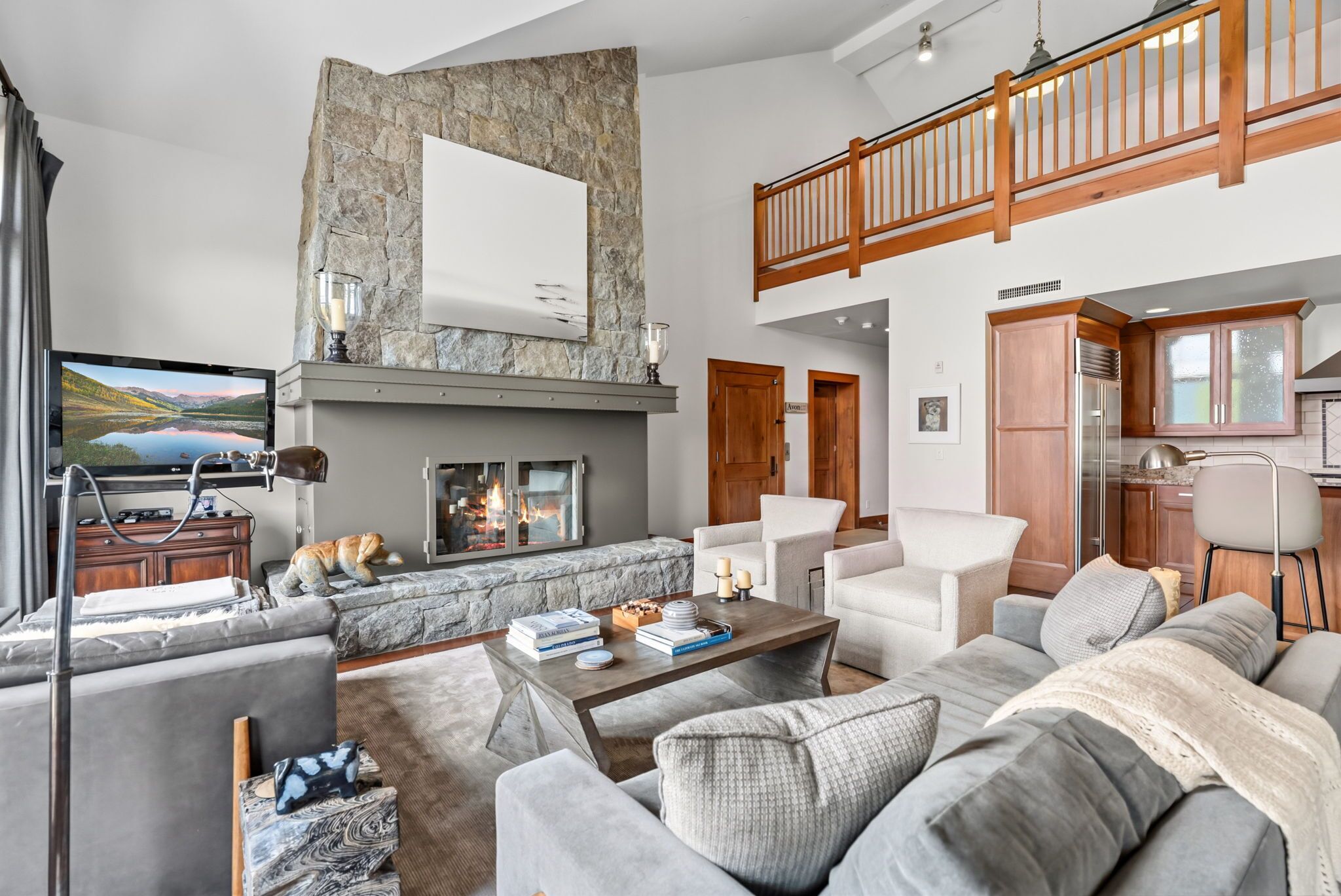 A spacious living room with a fireplace, a television, and a high ceiling with a wooden balcony.