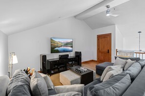 Ein modernes Wohnzimmer mit Flachbildfernseher, einer schwarzen Unterhaltungseinheit, einem grauen Sofa und einer Holztür.