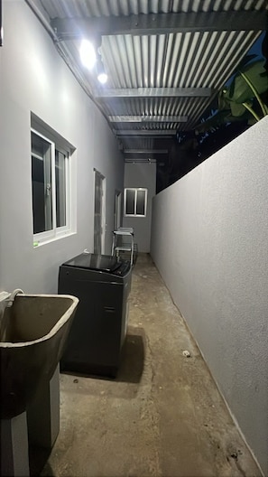 A narrow corridor with a trash bin, a window, and a metal structure on the ceiling.