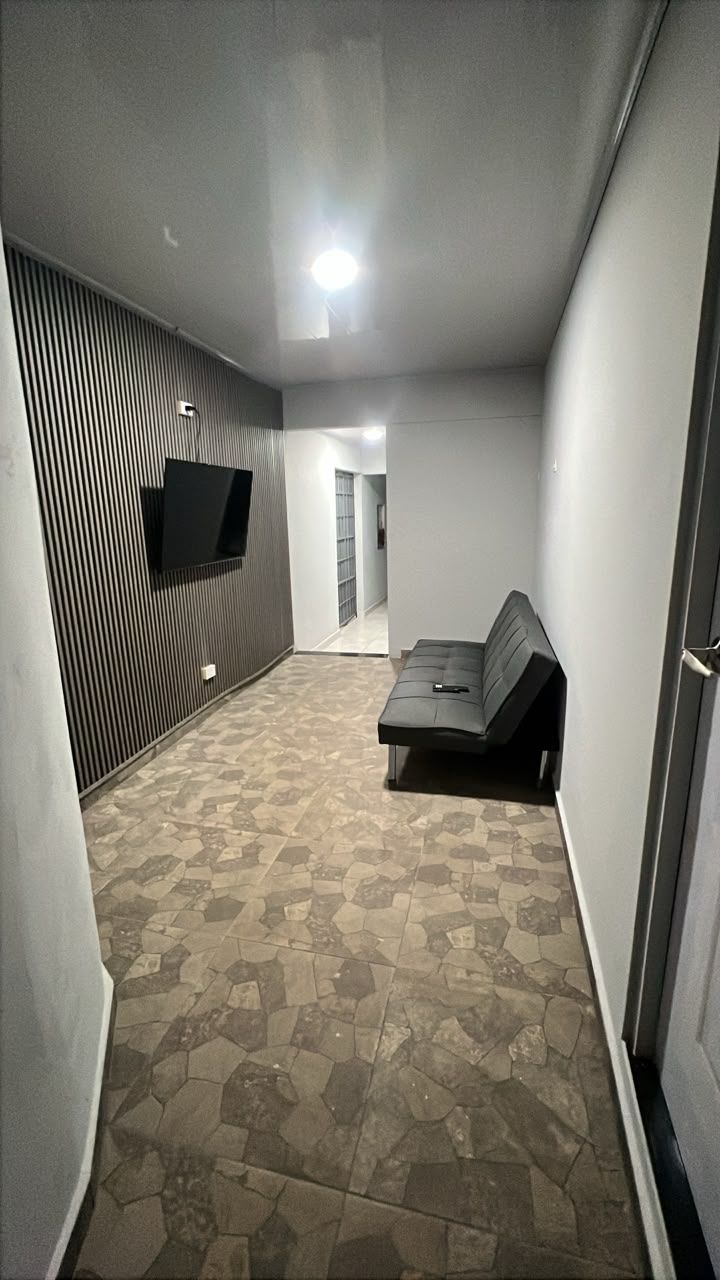 Um corredor com piso estampado, uma TV de tela plana na parede e um sofá ao fundo.