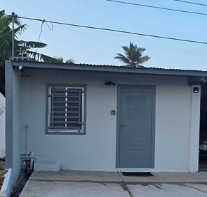 A small, single-story building with a grey door and window, a concrete floor, and a metal roof.