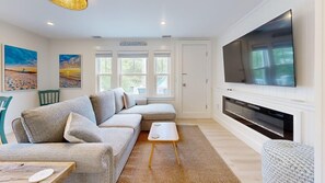 Ein Wohnzimmer mit Ecksofa, Flachbildfernseher, Kamin und Bildern an den Wänden.
