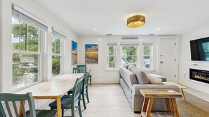 Ein modernes Wohnzimmer mit Essbereich, großen Fenstern, Kamin und Fernseher.