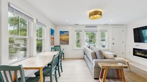 A modern living room with a dining area, large windows, a fireplace, and a television. - The Ultimate Group Escape on Marthas Vineyard (Oak Bluffs)