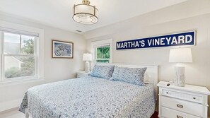 Une chambre à coucher avec un lit, une table de chevet, une lampe et un panneau mural sur lequel on peut lire « MARTHA’S VINEYARD ».