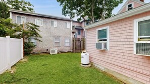 Une propriété résidentielle dotée d’une cour arrière clôturée, d’une cuve à gaz et d’une maison à la façade rose.