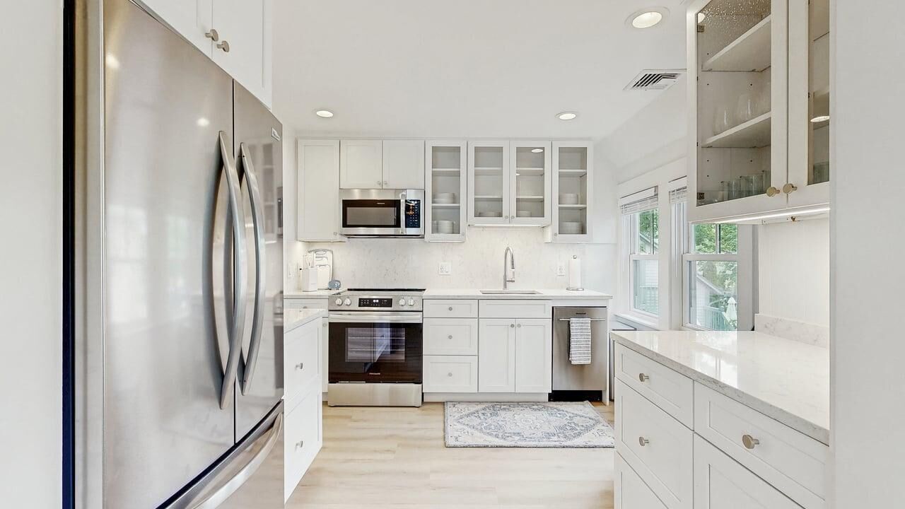 Una cocina moderna con electrodomésticos de acero inoxidable, armarios blancos y un ventanal que proporciona luz natural.