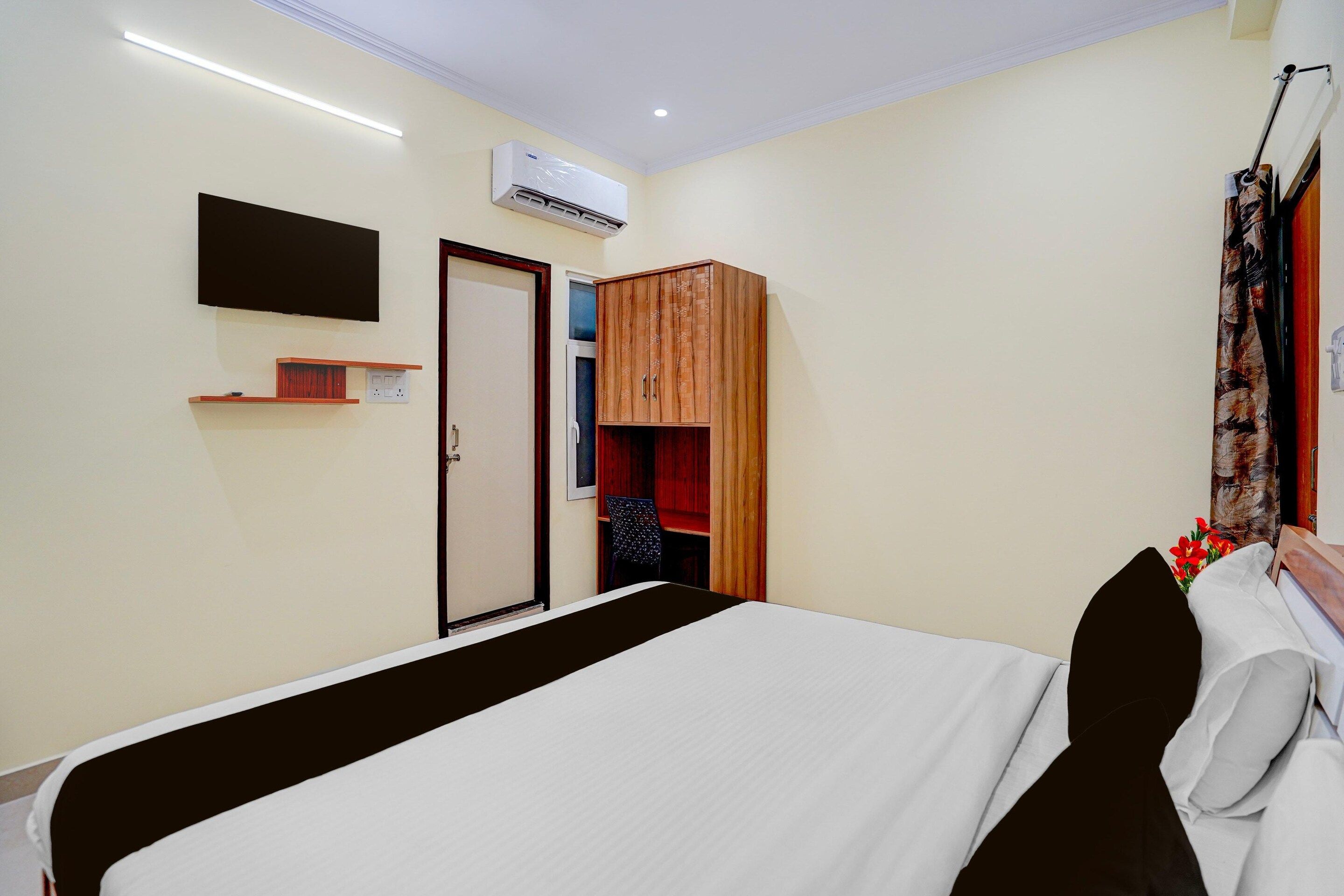 A hotel room with a bed, a wardrobe, a television, and an air conditioning unit.