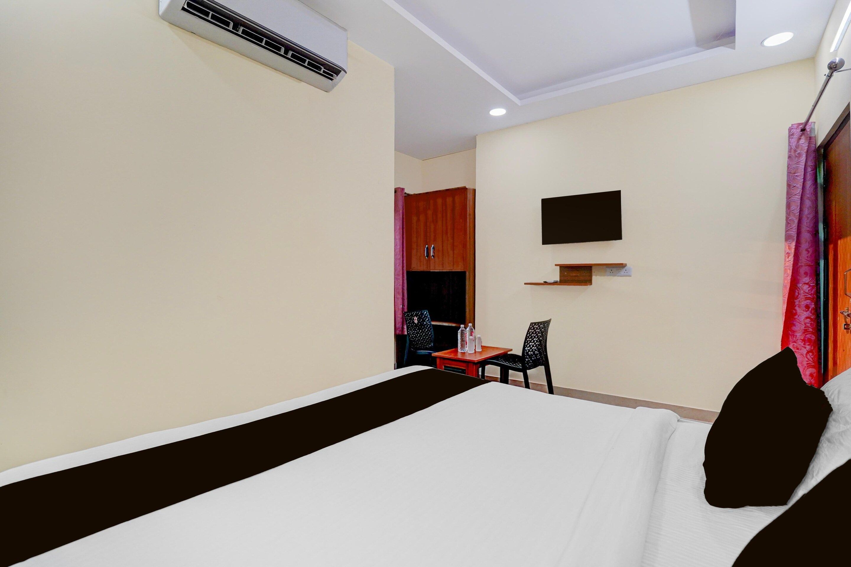 A hotel room with a bed, a desk, a chair, an air conditioning unit, a television, and a curtain.