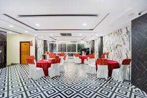 Sala de conferência com várias mesas e cadeiras, piso estampado e extintor de incêndio na parede.