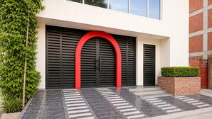Un edificio dal design moderno, con un'ampia porta nera ad arco rosso, un'area d'ingresso piastrellata e un muro in mattoni con un piccolo giardino.