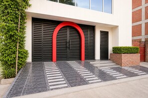 Ein Gebäude im modernen Stil, mit einer großen, schwarzen Tür und einem roten Bogen, einem gefliesten Eingangsbereich und einer Backsteinmauer mit einem kleinen Garten.