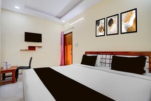 Ein Hotelzimmer mit einem Bett, einem an der Wand montierten Fernseher und drei gerahmten Kunstwerken darüber.