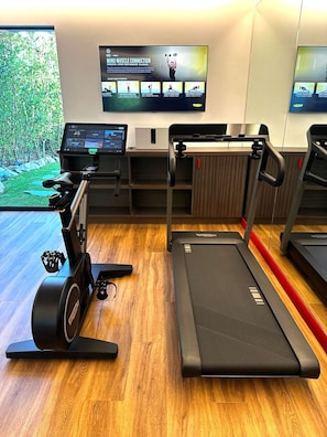 A gym with treadmills, a stationary bike, and a rowing machine. There is a TV screen displaying workout videos.