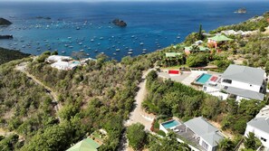 A coastal residential area with houses, a swimming pool, and a view of the sea with numerous boats.