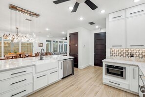 A modern kitchen with white cabinetry, a built-in oven, and a dining area with a chandelier. - Luxury Coastal Retreat | Pool, Golf Cart & Gulf Views (Panama City Beach)