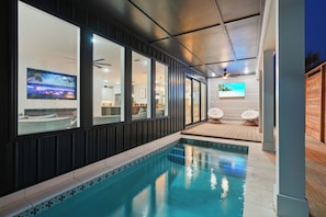 A modern indoor pool area with a clear view of the adjacent living space, including a kitchen and seating area.