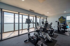 A gym with cardio machines and weight equipment, large windows with a view of the sea, and a sign indicating equipment for adult use only. - Golden Sands 706 by Seaside Vacations & Sales (Ocean City)