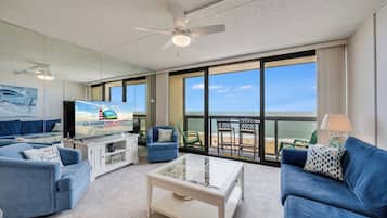 Una sala de estar moderna con televisor, sofás, una mesa de centro y un balcón con vista a la playa.