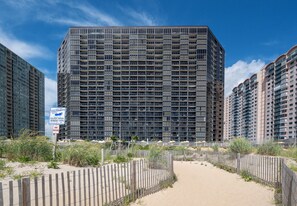 A high-rise building with multiple balconies, a sandy path in front, and a sign indicating a dune crossing. - Golden Sands 706 by Seaside Vacations & Sales (Ocean City)