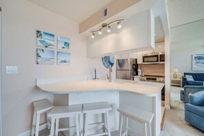 A modern kitchen with a central island, bar stools, and a dining area. - Golden Sands 706 by Seaside Vacations & Sales (Ocean City)