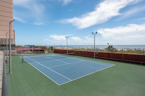Un court de tennis avec vue sur la plage et l’océan.