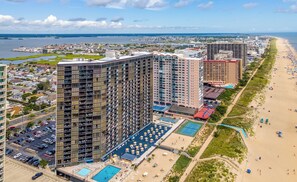 A high-rise hotel with multiple floors, a swimming pool, and a beach area with umbrellas. - Golden Sands 706 by Seaside Vacations & Sales (Ocean City)