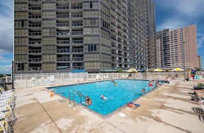 Une piscine entourée d’une clôture blanche, avec un grand immeuble en arrière-plan.