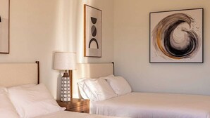 A hotel room with two beds, a nightstand with a lamp, and artwork on the walls.