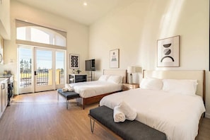 Habitación de hotel con dos camas, un escritorio, televisión y balcón con vistas.