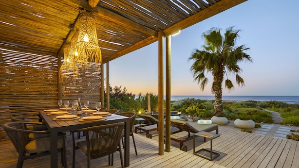 An outdoor dining area with a wooden deck, tables set for dining, and a view of the sea.