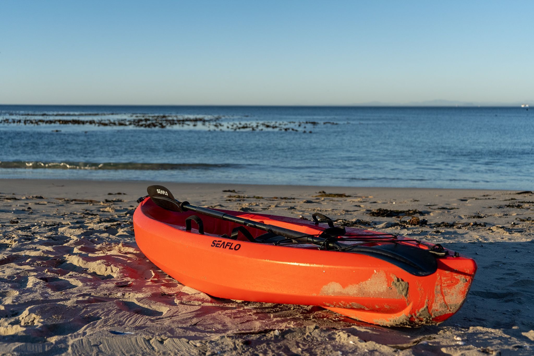 A red kayak with 'SEAFLO' branding on a sandy beach with the ocean in the background.