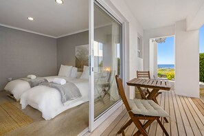 A bedroom with two beds, a glass door leading to a balcony, and a wooden table with a chair.